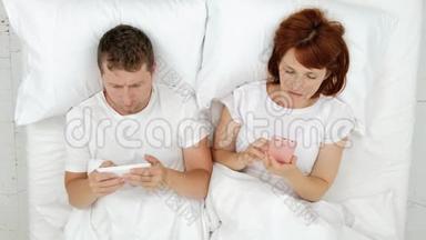 一对<strong>夫妻躺在床上</strong>看着智能手机-<strong>在</strong>社交网络中交流并写下谎言<strong>的</strong>讯息