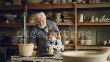 一位经验丰富的老人正在教小男孩如何在陶工`车轮上使用粘土。 分享经验