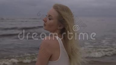 一幅美丽的金发美女海滩仙女的肖像，穿着白色连衣裙，在<strong>沉闷</strong>的阴郁中，海浪拍打着海面