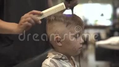 理发店里有吹风机的男孩发型。 理发店的儿童理发。 理发师发型小男孩与