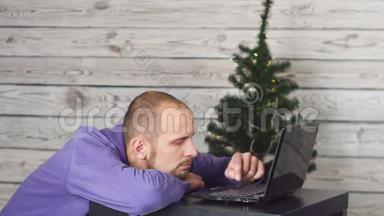 年夜在办公室里累得昏昏欲睡的商人。 办公室里的圣诞树。 桌子上有笔记本电脑。 商业概念。 男子