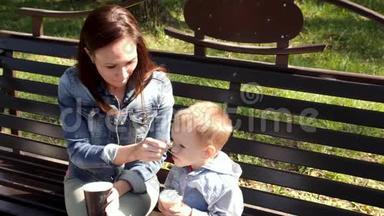 年轻的妇女和孩子正在公园的长凳上吃<strong>冰淇淋</strong>。年轻的母亲用勺子给儿子吃<strong>冰淇淋</strong>。慢