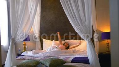 年轻漂亮的女人醒来在白色的床上伸<strong>展</strong>和快乐的跳跃在卧室。 3840x2160
