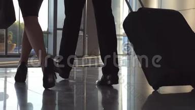 商务人士带着行李通过自动玻璃门离开机场。 年轻男女穿着<strong>高跟鞋走路</strong>
