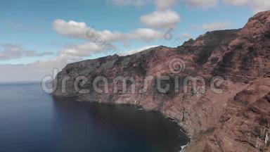 空中射击。 巨大的黑红色火山岩的海岸是海洋蓝色水域中的一座山。 与蓝色对抗