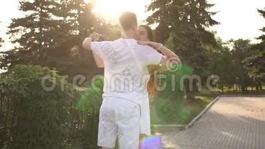 快乐的年轻情侣在公园日落时跳着慢华尔兹。