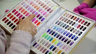 女人选择一种颜色在美容院画指甲。 各种颜色的指甲油测试仪的集合..