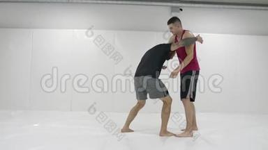 希腊罗马摔跤手在一个有垫子的白色房间里。 练习自卫技巧。 投掷和疼痛