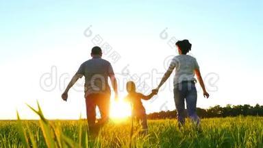 幸福的年轻家庭，一个孩子在绿色的草坪上奔跑，手牵着夕阳背景，慢悠悠地走着