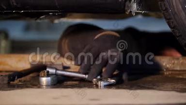 汽车服务。 厚厚的机械师躺在车下，用手寻找工具。 带着一个钳子