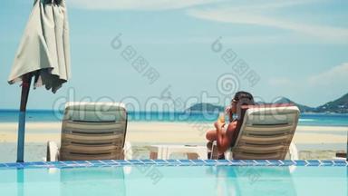 美丽的年轻女子在海滩休息室用她的手机喝鸡尾<strong>酒</strong>，同时进行日光浴。 3840x2160
