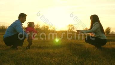 爸爸妈妈和孩子在日落时在草地上玩。 家庭幸福的概念。 宝宝从爸爸到妈妈都在草坪上。 儿童