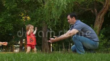 小女儿迈出第一步，在公园的草坪上遇见笑着的爸爸。 爸爸亲吻婴儿的脸颊和微笑。 慢慢