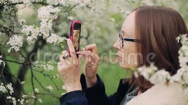 偶然的女人在智能手机上拍摄春天的花朵。