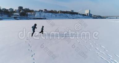 妈妈和太阳在雪地里<strong>一起跑</strong>步和玩耍。 空中镜头。 冬天的家庭消遣。