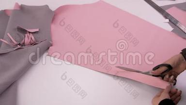 裁缝用剪刀剪粉红色的布料来缝制运动衫。 裁剪布料。