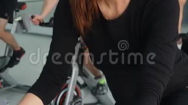 健身妇女在自行车课上进行室内自行车训练。 团体运动的人在自行车健身房旋转自行车。 心脏培训
