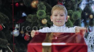 快乐的微笑男孩展示了红色`新年礼物。 小孩站在圣诞树<strong>下</strong>