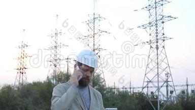 站技术负责人戴着白色安全帽站在电站附近，与工人通电话..