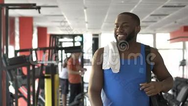 肌肉发达的非裔美国人，脸上带着微笑走在健身房里，遇见朋友
