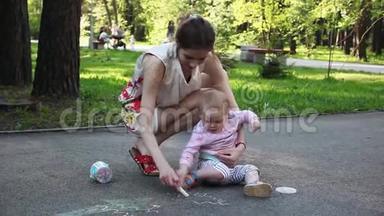 可爱的小女孩和她的母亲在夏天公园的人行道上用粉笔画画。 家庭、母亲和人的概念