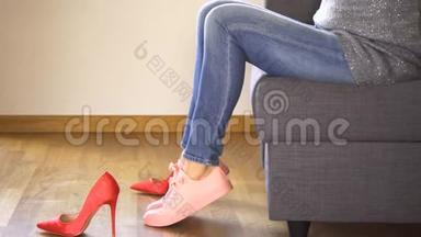 在沙发上穿牛仔裤的苗条女人脱掉<strong>红色高跟鞋</strong>，穿上珊瑚运动鞋
