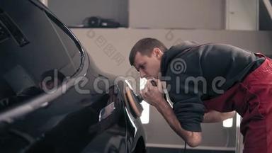 汽车中心的年轻男工人照看着一辆黑色昂贵的汽车，用磨砂机抛光。擦<strong>亮眼</strong>睛。
