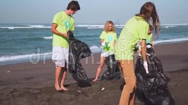 四名志愿者穿着绿色T<strong>恤衫</strong>，带着图像回收，在海滩上收集垃圾，拿着收集的袋子在镜头前看