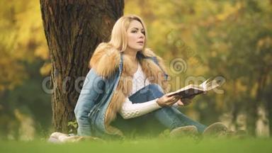 时尚的女士在中央公园阅读冒险书，坐在树下，秋天