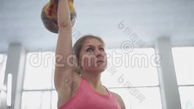 年轻女子运动员表演一个挺举的水壶铃。 健身房里的女孩用水壶做健身运动