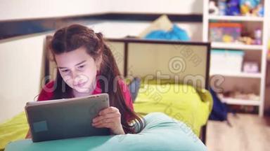 躺在床上玩数码平板电脑的小女孩。小女孩玩数码平板电脑小女孩坐在床上