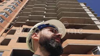 施工经理戴着安全帽，留着胡子和胡子在高层建筑的背景上。 4k