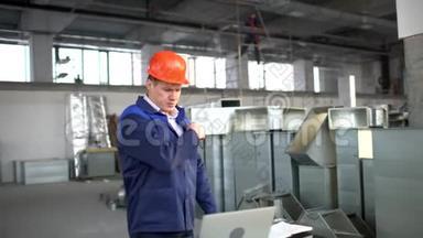 戴着安全帽的工厂工人正在使用带有工程软件的笔记本电脑。 空调和空调风管