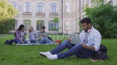 混合种族学生在笔记本电脑上上网聊天，坐在大学附近的草地上