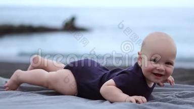 婴儿趴在海边的黑沙上，笑着看着摄像机