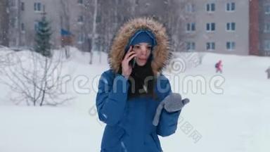 冬天降雪时，年轻漂亮的女人在户外打电话。