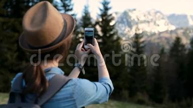 有魅力的女孩旅行者在山上的背景下用手机拍照。 为游客拍照