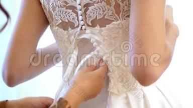 特写，新娘费用.. 新娘为婚礼穿衣服。 伴娘用丝带系上白色花边连衣裙。 婚礼