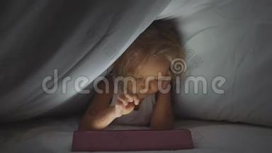 小可爱的女孩躺在羽绒被下，睡觉时使用数字平板设备。