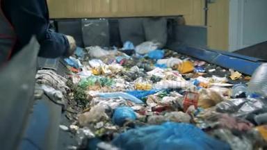 垃圾回收厂。 一个戴手套的人从废物分类工厂的移动线路中挑选不可回收的垃圾。