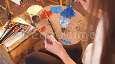 女艺术家拿着调色板与蓝色和红色的油彩和绘画图片特写。