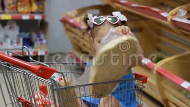 小女孩坐在超市的<strong>手推车</strong>里吃东西，拿着面包。 <strong>婴儿</strong>购物