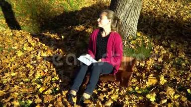 一个年轻漂亮的十几岁的女孩坐在秋天森林的一棵树<strong>下</strong>读一本书。 她做梦。 女孩很安详