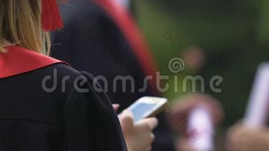 女<strong>大学毕业</strong>生在智能手机上打字和发送信息的背面视图