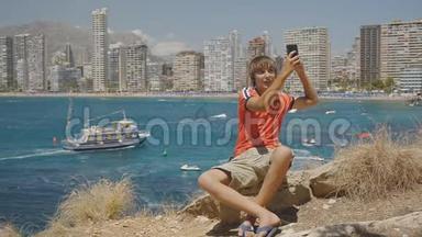 白种人少年在智能手机上打视频电话，展示海上海岸和摩天<strong>大楼</strong>天际线背景。