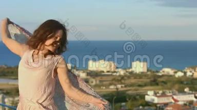美丽的幸福女人带着围巾跳舞，背景中的海洋景观令人惊叹