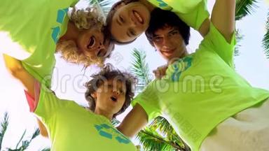 四名年轻志愿者身穿绿色t恤衫，照片上的是一个海滩上棕榈树下的一个小丘