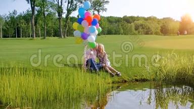 一对美丽的情侣拿着五颜六色的气球坐在河岸上的慢动作视频