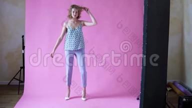 在一个粉色背景<strong>的</strong>摄影棚里，一个开朗、<strong>积极向上的</strong>金发女孩在为照相机摆姿势