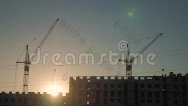 日落时吊车及建筑施工现场.. 剪影工人在天空的背景上。